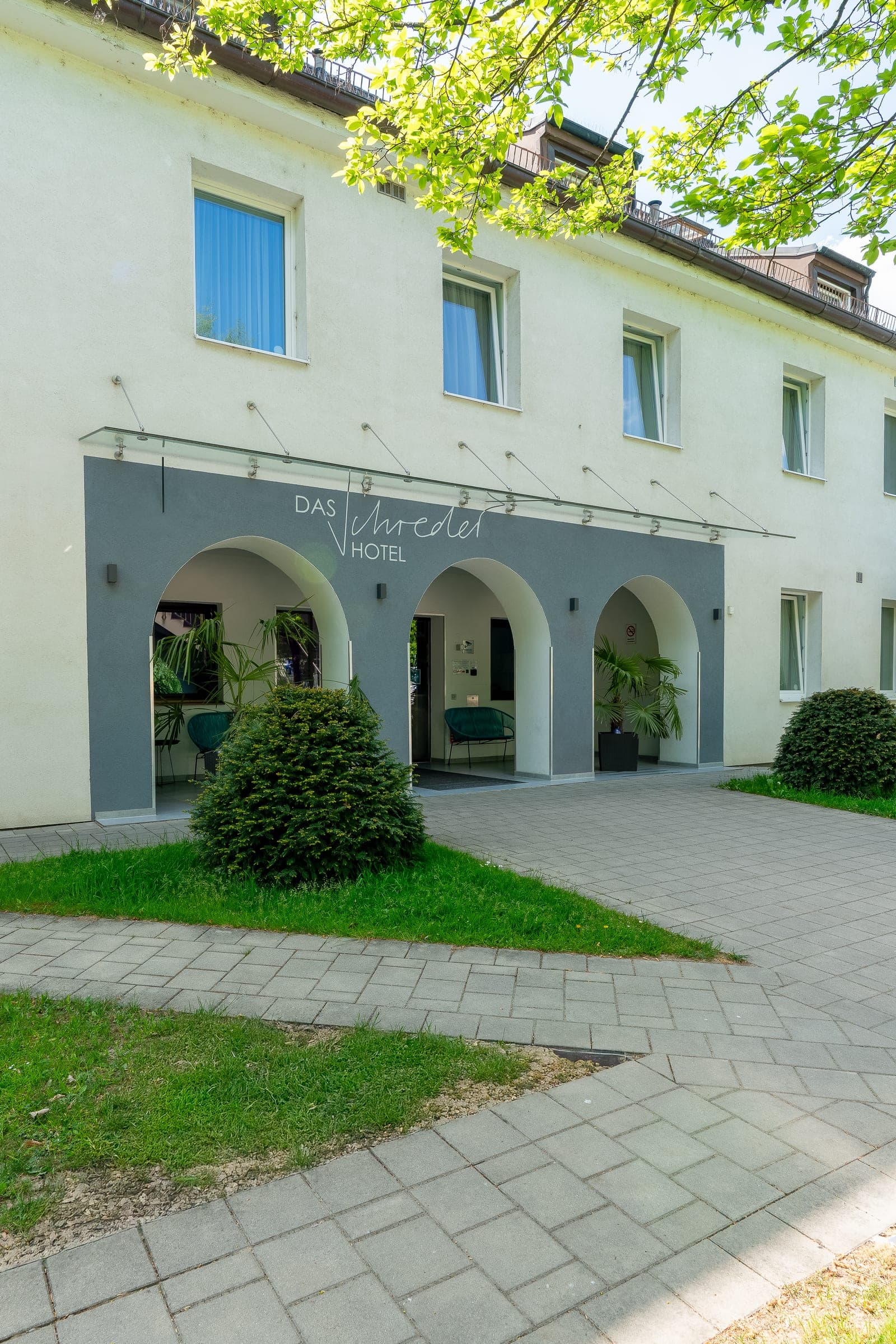 Das Schreder Hotel von außen: heller Bau mit dem Eingang unter den Rundbögen, davor Rasen und Bäume