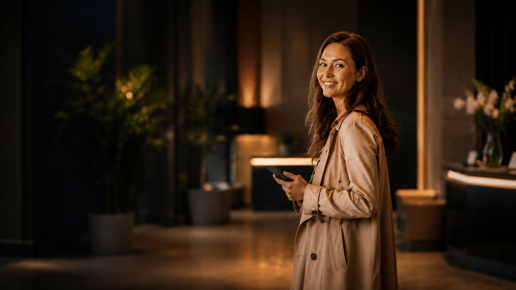 Lächelnde Frau mit Smartphone in einer warm beleuchteten Hotellobby