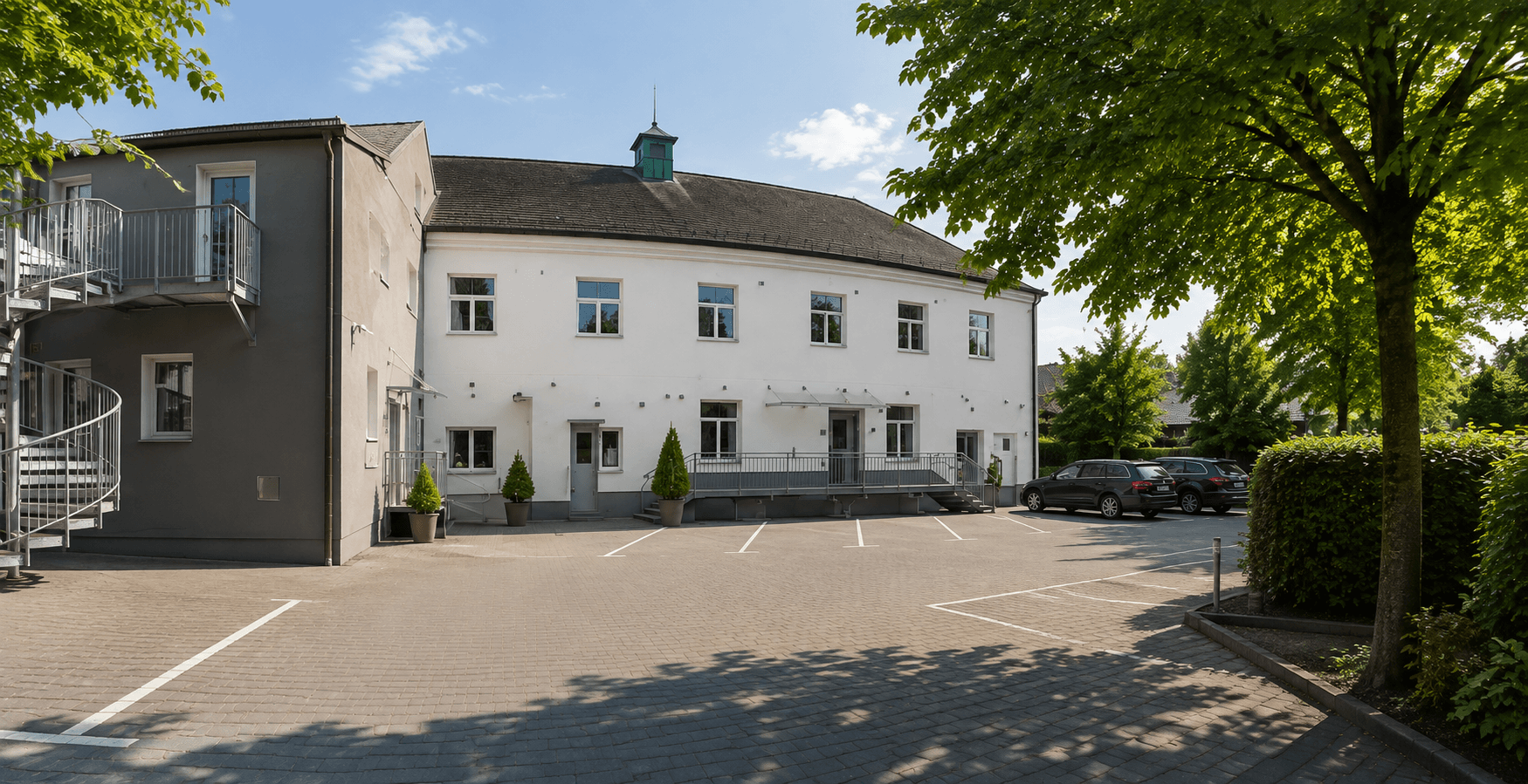 Der Parkplatz am Das Schreder Hotel bei Tageslicht mit markierten Stellplätzen vor dem weißen Gebäude